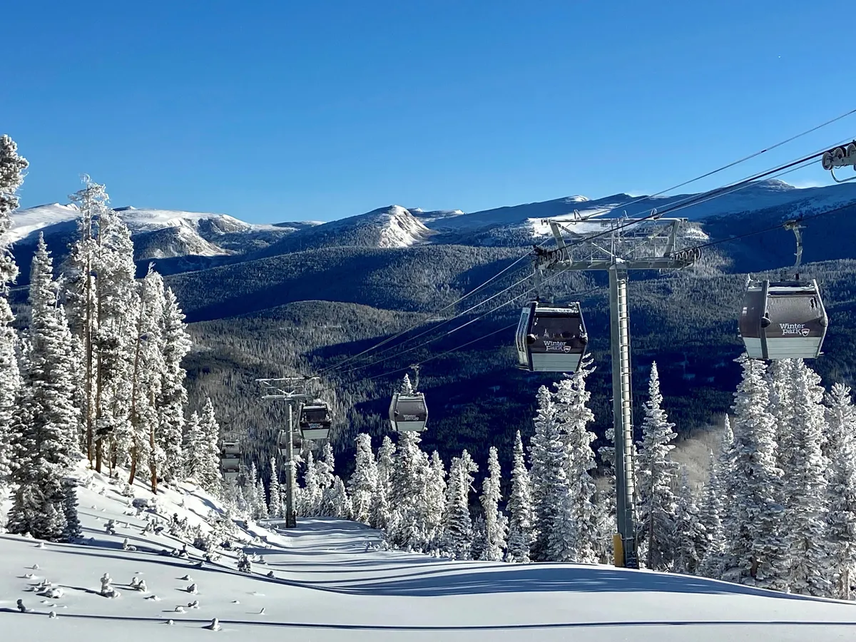 This image captures ski lift gondolas gliding above snow-covered trees with a majestic mountain range in the background, evoking the thrill and accessibility of ski-in/ski-out adventures right outside the door.