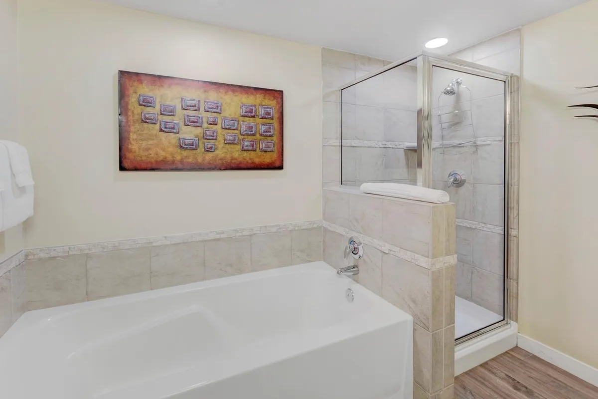 A modern bathroom featuring a spacious bathtub, sleek shower enclosure, and elegant framed artwork. The design exudes a spa-like ambiance ideal for relaxation and self-care.