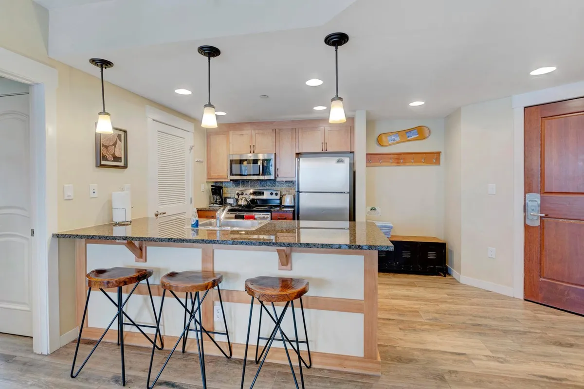 A spacious, modern kitchen anchored by a large island with bar stools, shining stainless steel appliances, and a granite countertop. The setup suggests a seamless flow for preparing and sharing meals, while the bar stools invite casual conversation or quick breakfasts. The organized space is warm and inviting, perfect for family gatherings or entertaining guests.