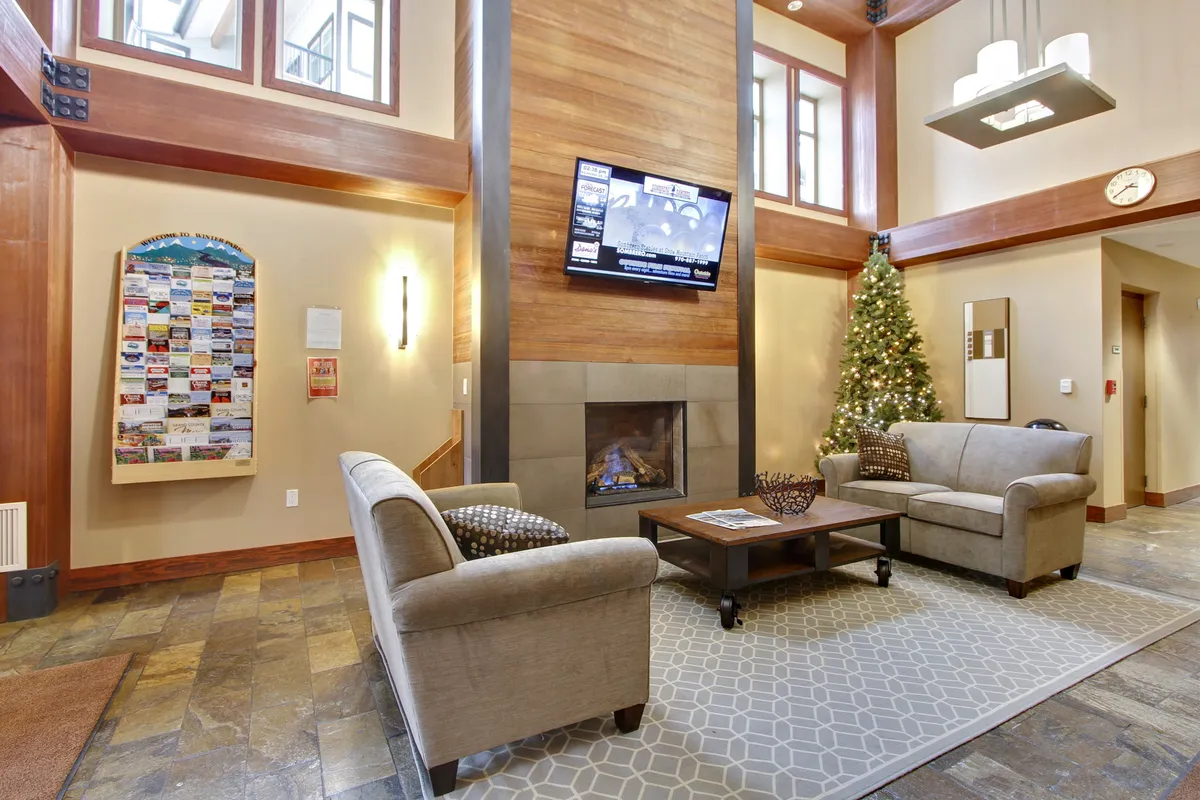 A beautifully appointed lobby space with a grand fireplace, cozy seating areas, a Christmas tree, and an information board. The atmosphere is warm and inviting, perfect for social gatherings, relaxing by the fire, or planning the day's adventures.