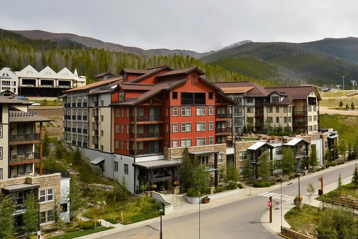 This image presents a welcoming multi-story building set against a dramatic mountain backdrop, with a landscaped entryway that invites guests toward the property. Balconies offer views into the surrounding scenery, hinting at both privacy and connection to the outdoors. The soft lighting and natural surroundings evoke a sense of peaceful retreat and relaxation.